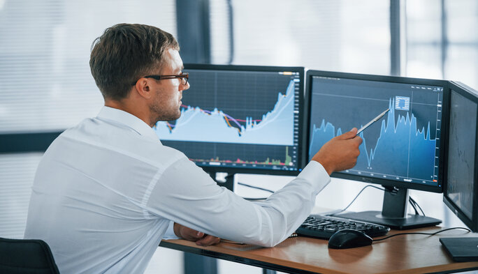 Monitoring information. Young businessman in formal clothes is in office with multiple screens. Conception of exchange and money